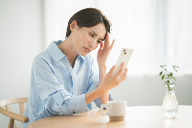 考えながらスマートフォンを見ている女性